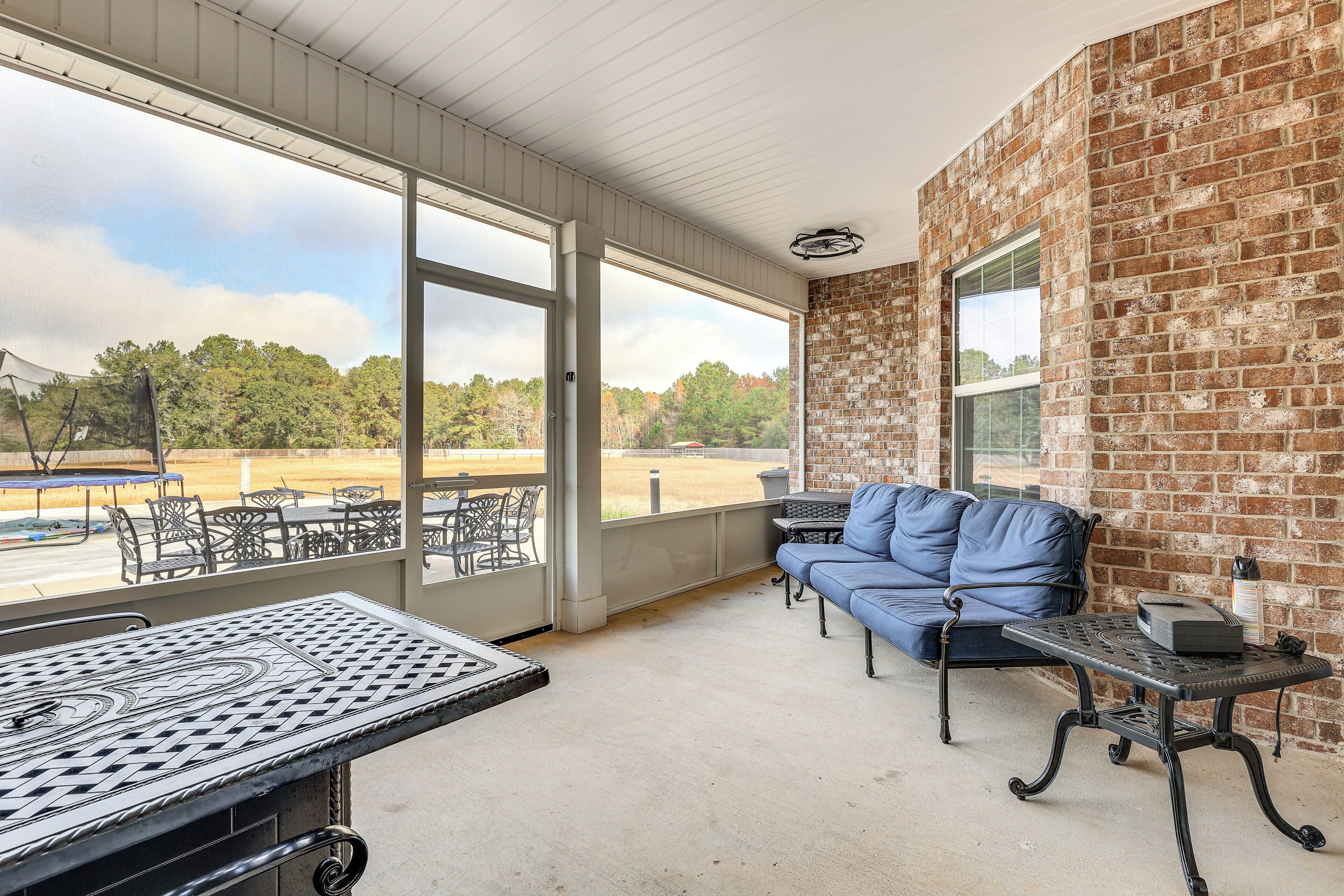 A covered patio with a brick wall, a blue sofa, a table, and a view of a field.