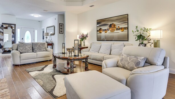 Un salon spacieux avec un plafond haut, un ventilateur de plafond et un grand tableau. On y trouve deux canapés et une table basse agrémentée d’objets décoratifs.