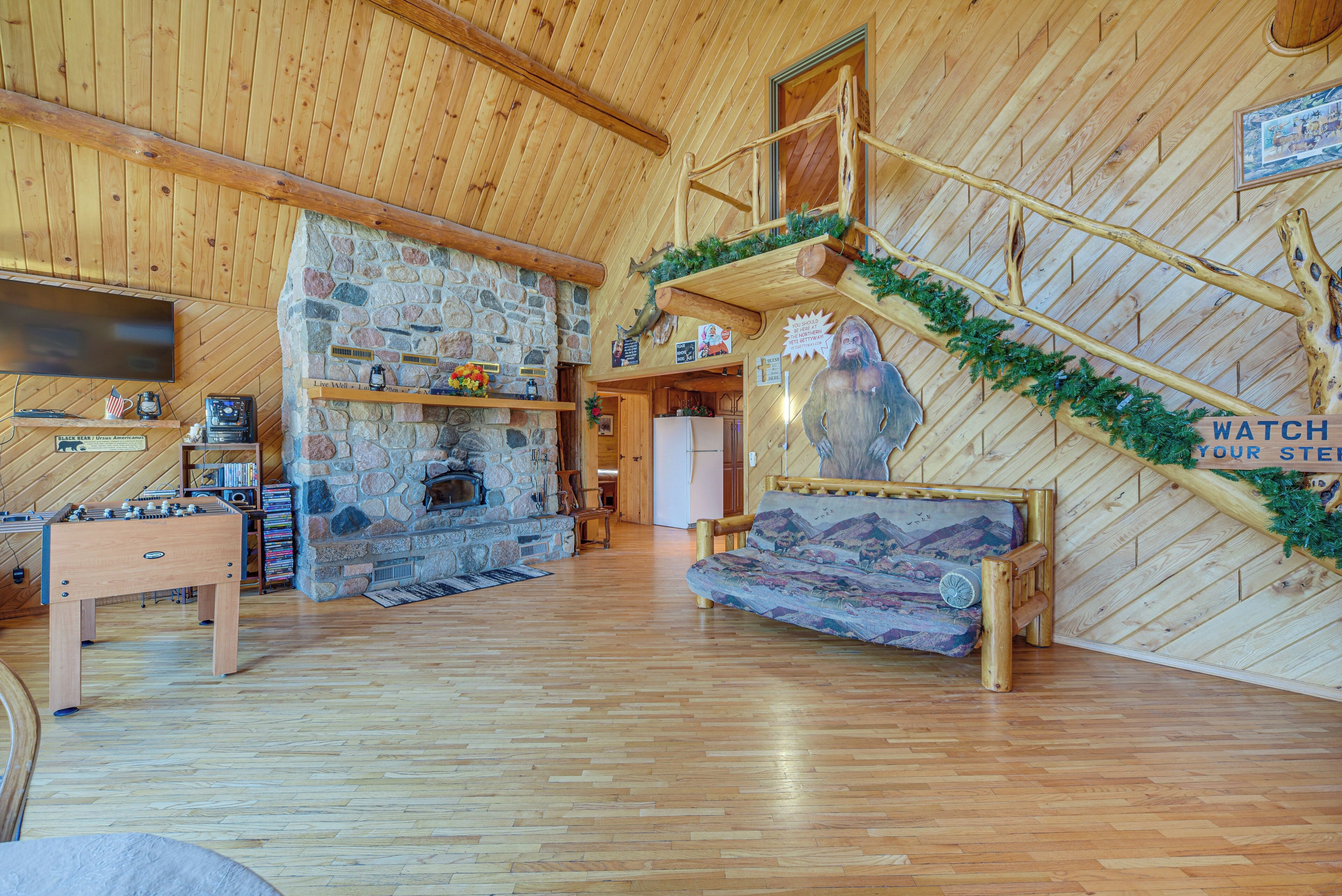 Interior acogedor de una cabaña con chimenea de piedra, muebles de madera y una escalera de madera.