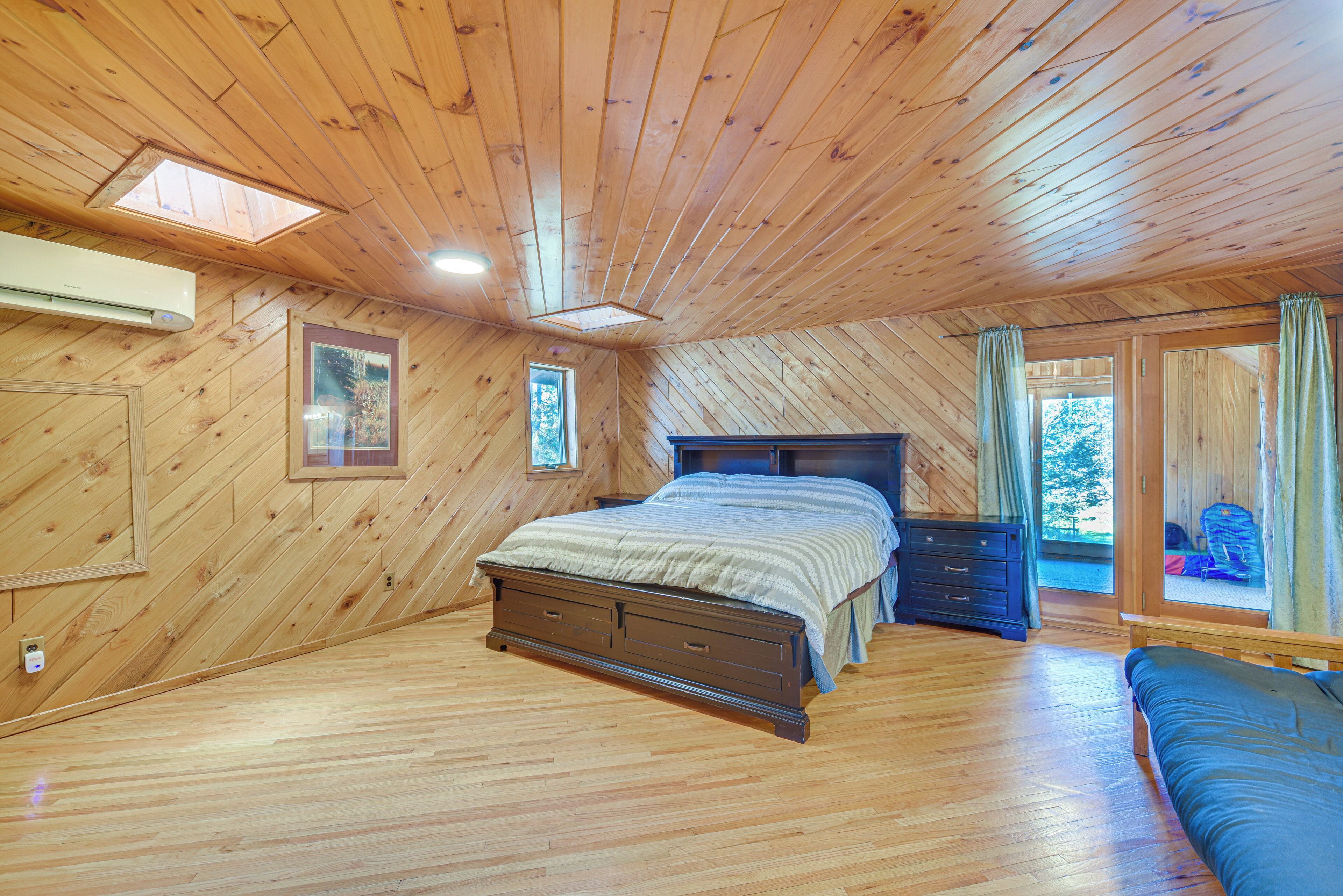 A wooden-paneled bedroom with a bed, dresser, and a view of the outdoors.