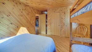 Una habitación de cabaña de madera con literas, techo de madera y un armario con puertas.
