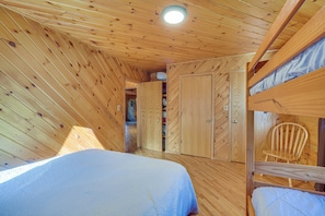 A wooden cabin room with bunk beds, a wooden ceiling, and a closet with doors.