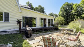 A covered patio area with stone flooring, outdoor furniture, and a view of a yellow house with large windows. - Perfect Family Retreat: Pool, Fire Pit (Westfield)