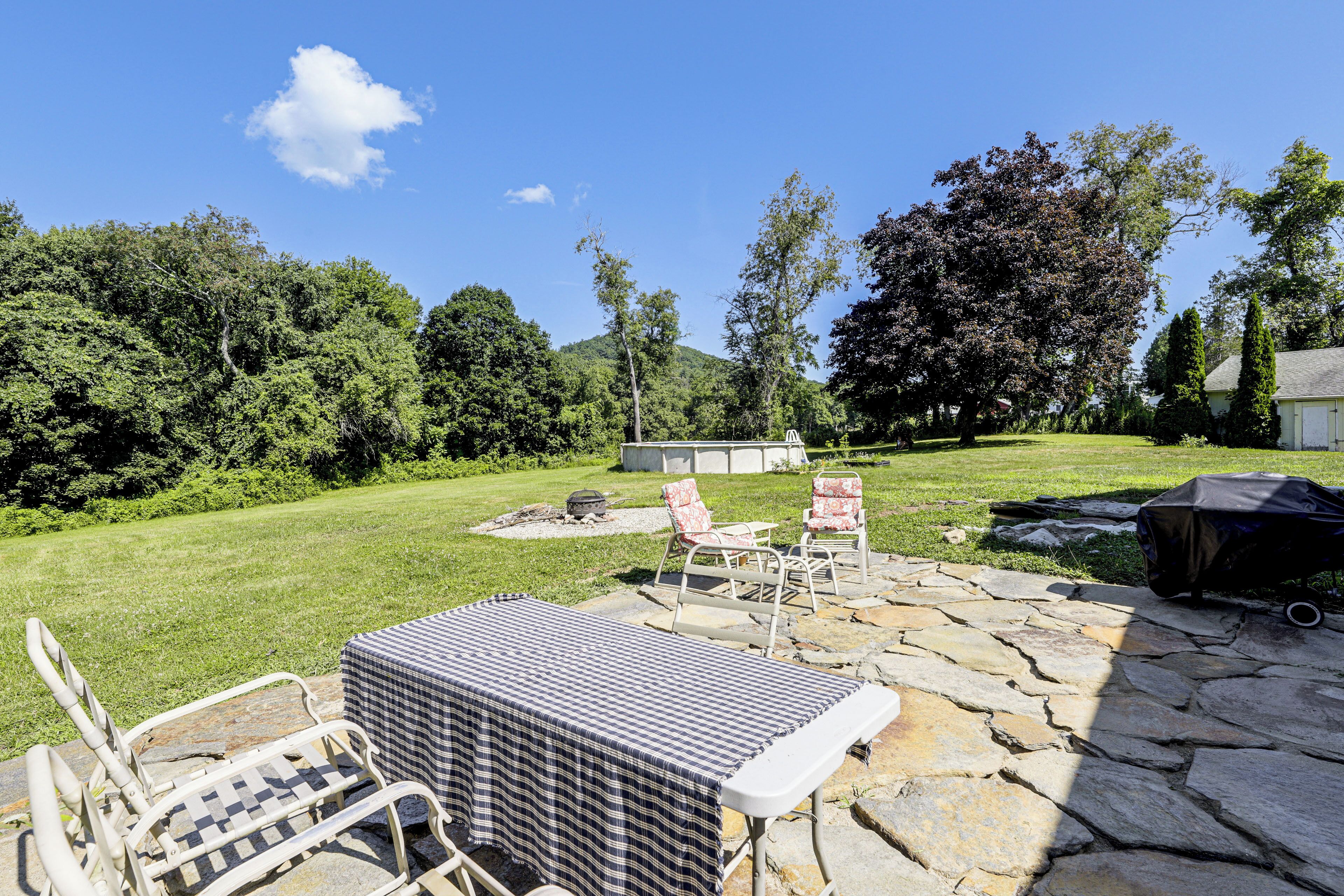 A stone patio with outdoor furniture, a grill, and a view of a lush green landscape with trees.