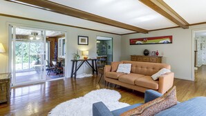 A spacious living room with a wooden floor, a sofa, a dining table, and a view through a glass door. - Perfect Family Retreat: Pool, Fire Pit (Westfield)