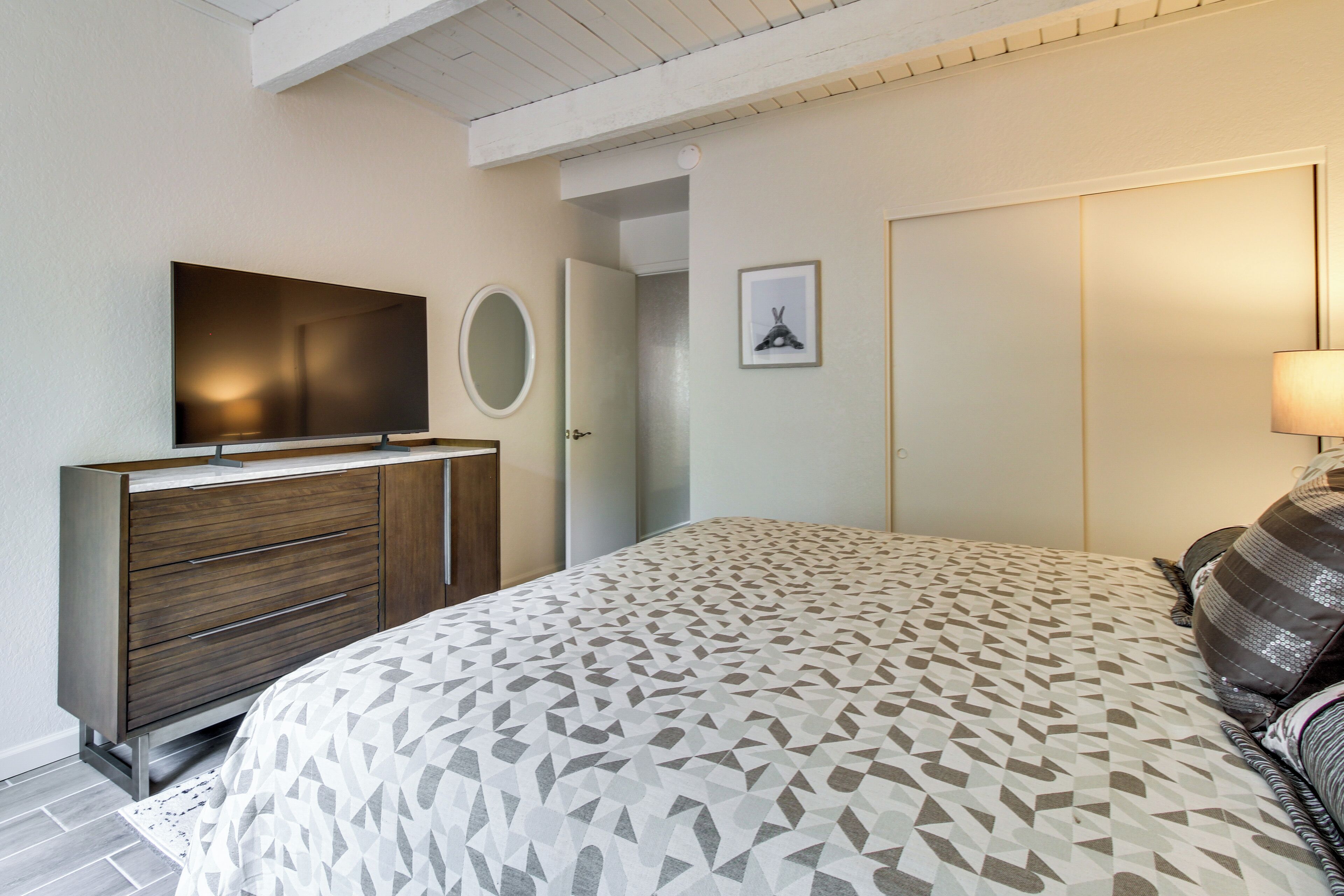 A bedroom with a bed, a TV on a cabinet, a door, and a framed picture on the wall.