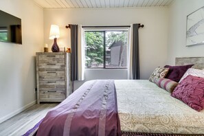 Ein Schlafzimmer mit einem Bett, einem Schminktisch, einer Lampe, einem Fenster mit Vorhängen und Blick nach draußen.