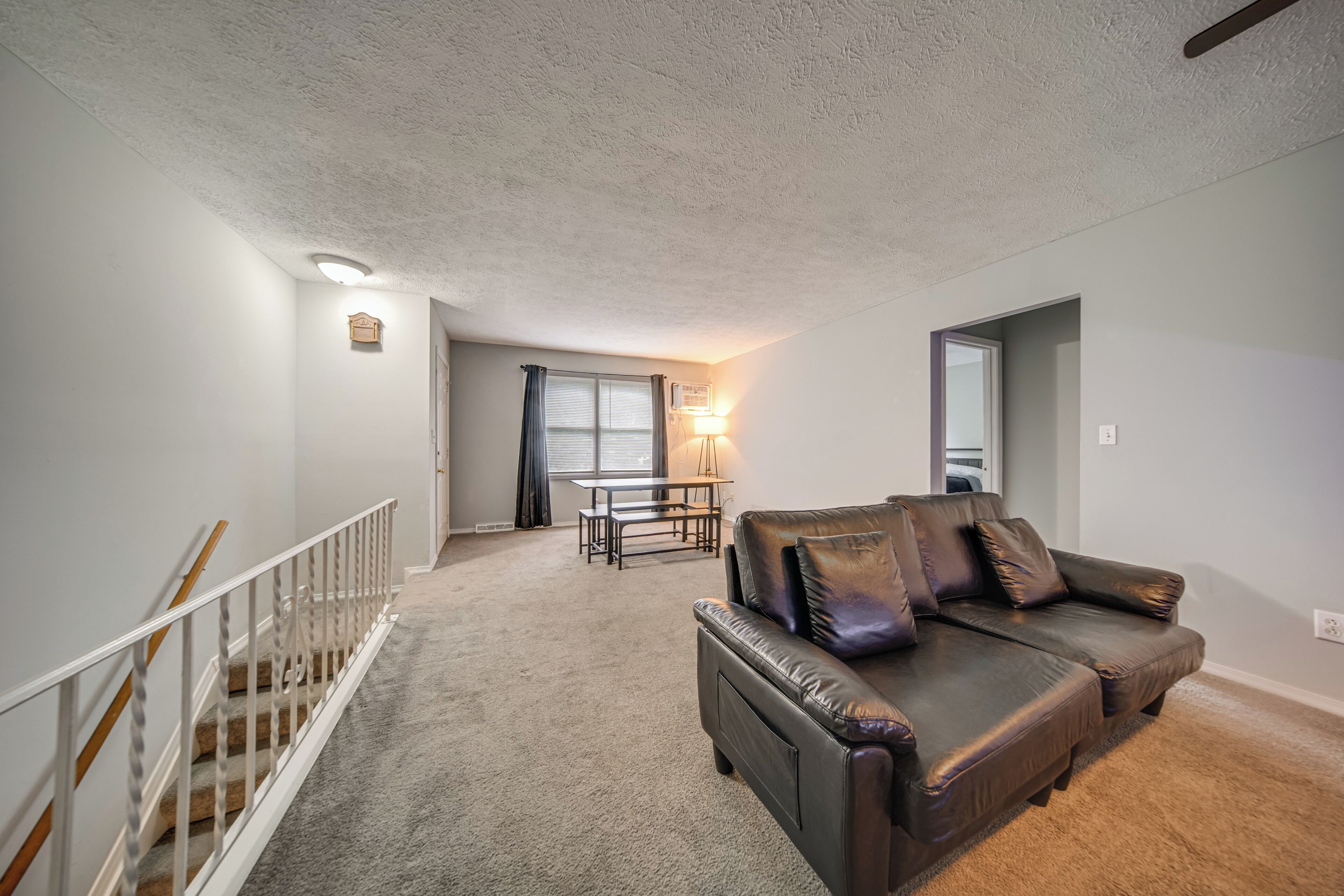 A living room with a leather sofa, a dining table with chairs, a staircase, and a ceiling light fixture.