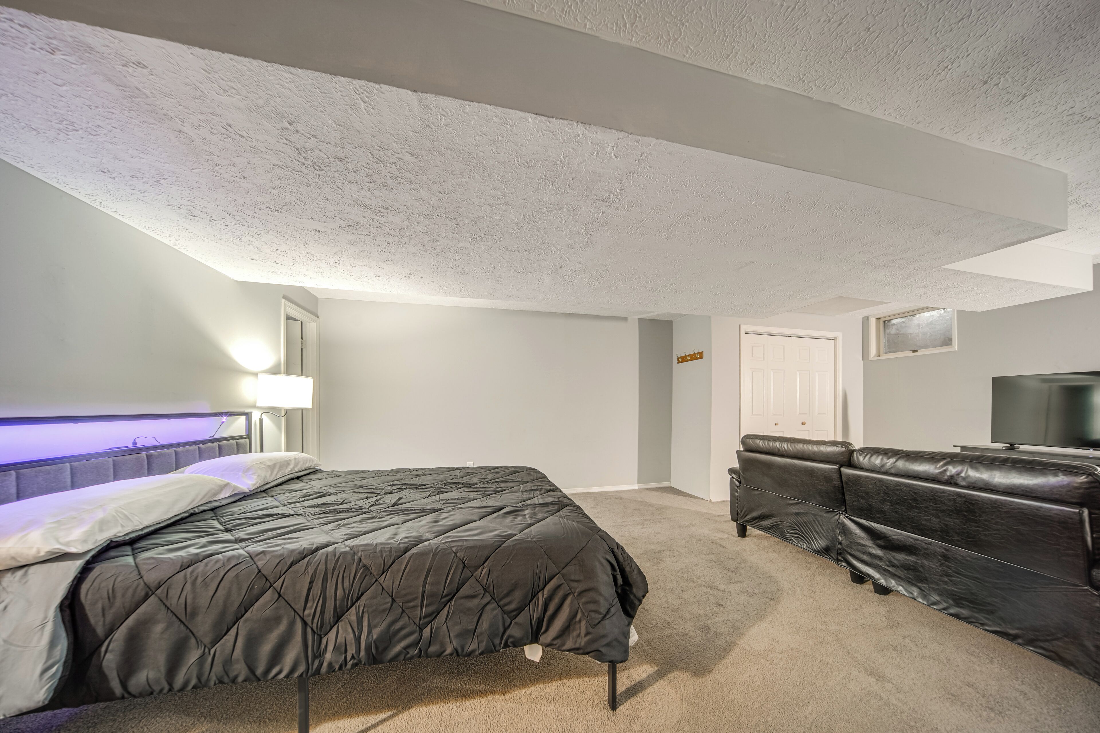 A bedroom with a bed, a television, a leather couch, and a carpeted floor.