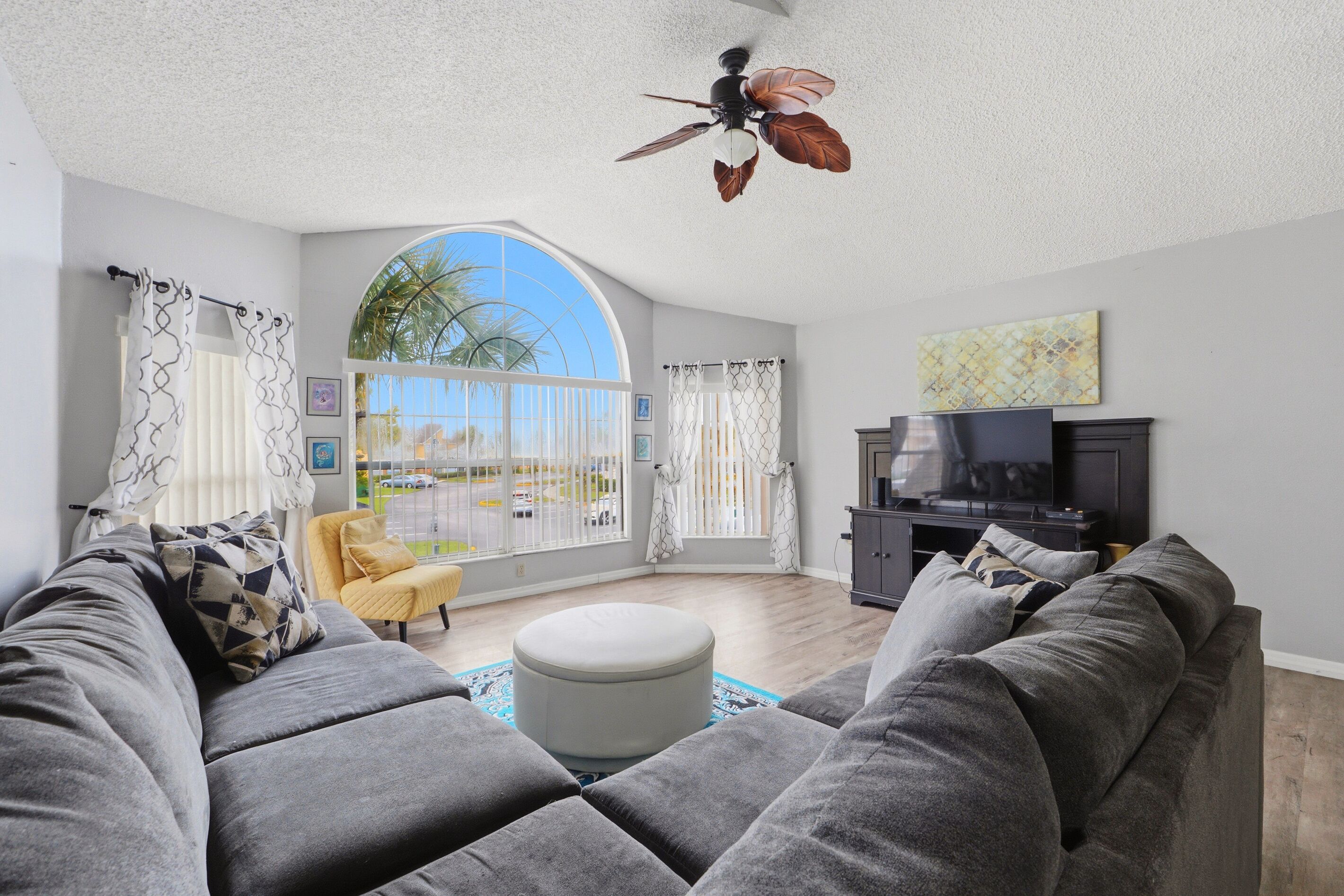 A living room with a large window, a ceiling fan, a sofa, a TV, and a cabinet.