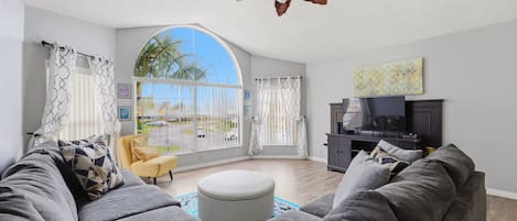 A living room with a large window, a ceiling fan, a sofa, a TV, and a cabinet.