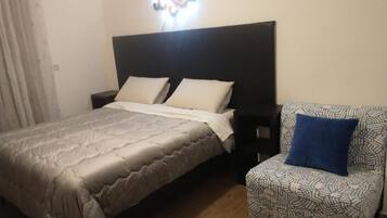 Una camera da letto con un letto, un comodino, una poltrona con motivo e un punto luce a parete.