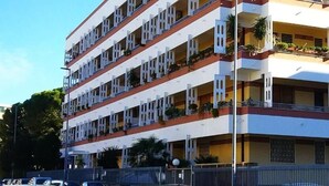 Ein mehrstöckiges Hotel mit Balkonen, einer flachen Dachterrasse und einem umzäunten Grundstück.