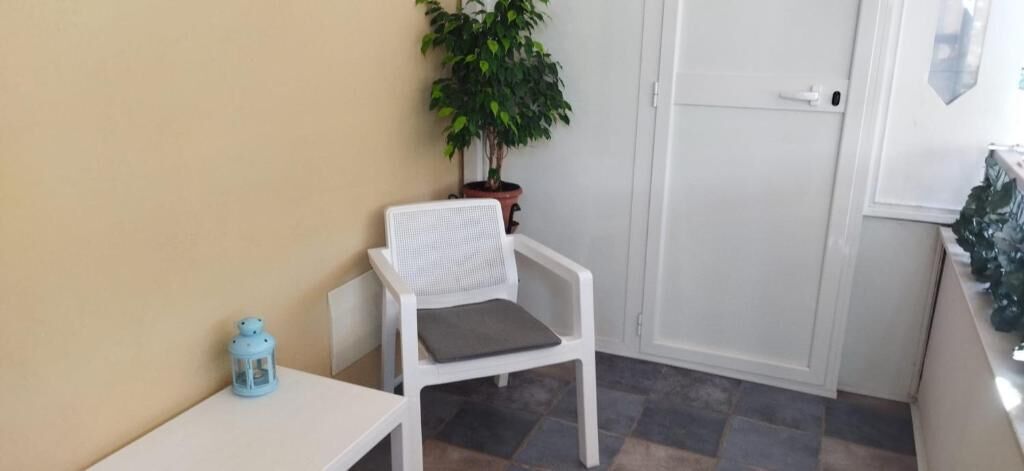 Una stanza piccola con una sedia bianca, un tavolino, una pianta in vaso e una porta.