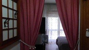 Ein Zimmer mit einem Bett, einem Fernseher und einem Fenster mit Vorhängen.