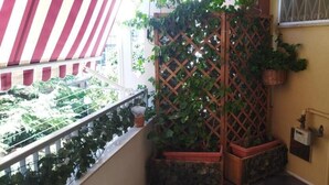 Ein Balkon mit einer rot-weiß gestreiften Markise, einem Holzziergitterwerk mit Pflanzen und einer T ür mit einem Metallgitter.