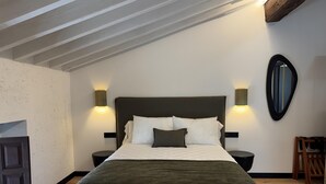 A bedroom with a large bed, two bedside tables, a mirror, and a wooden chair.