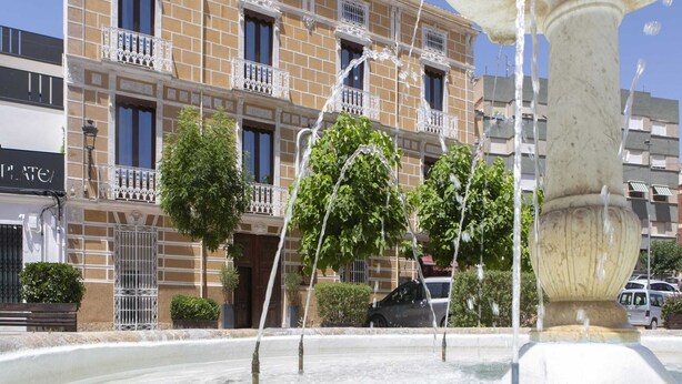 A fountain with water jets in front of a building with balconies and a sign that reads 'PLATE'.