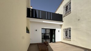 A modern outdoor patio with a wooden bench, a glass door entrance, and decorative metalwork on the walls.