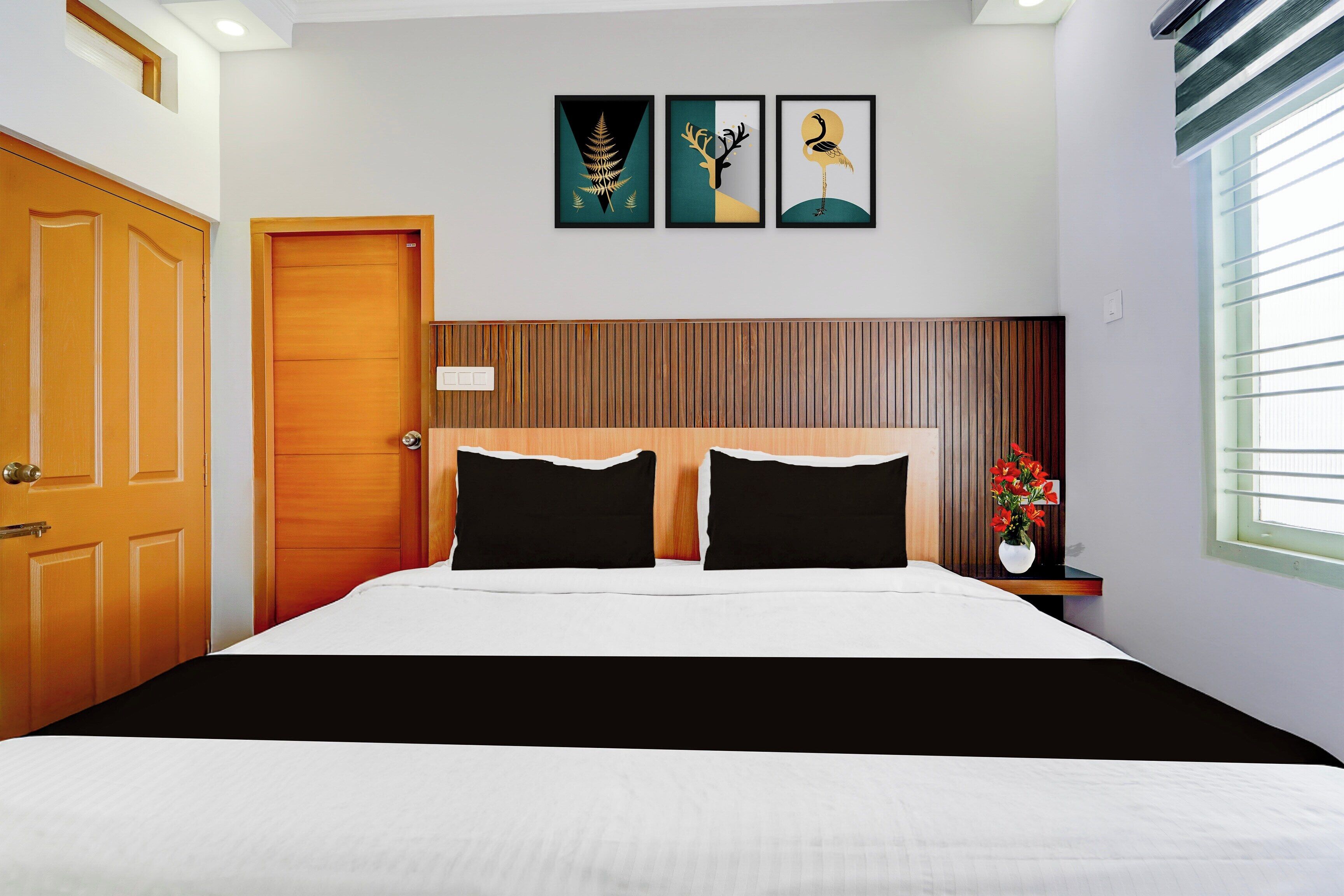 A bedroom with a wooden door, a bed with black and white bedding, and a window with blinds.