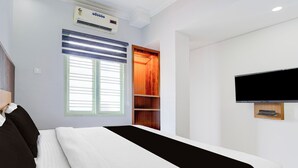 Ein Hotelzimmer mit Bett, Wandfernseher, Klimaanlage, Fenster mit Jalousien und einer eingebauten Ablagefläche.