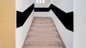 Eine Treppe mit schwarz-weißem geometrischen Wandmuster, die zu einer Zwischenebene mit einem kleinen Fenster führt.
