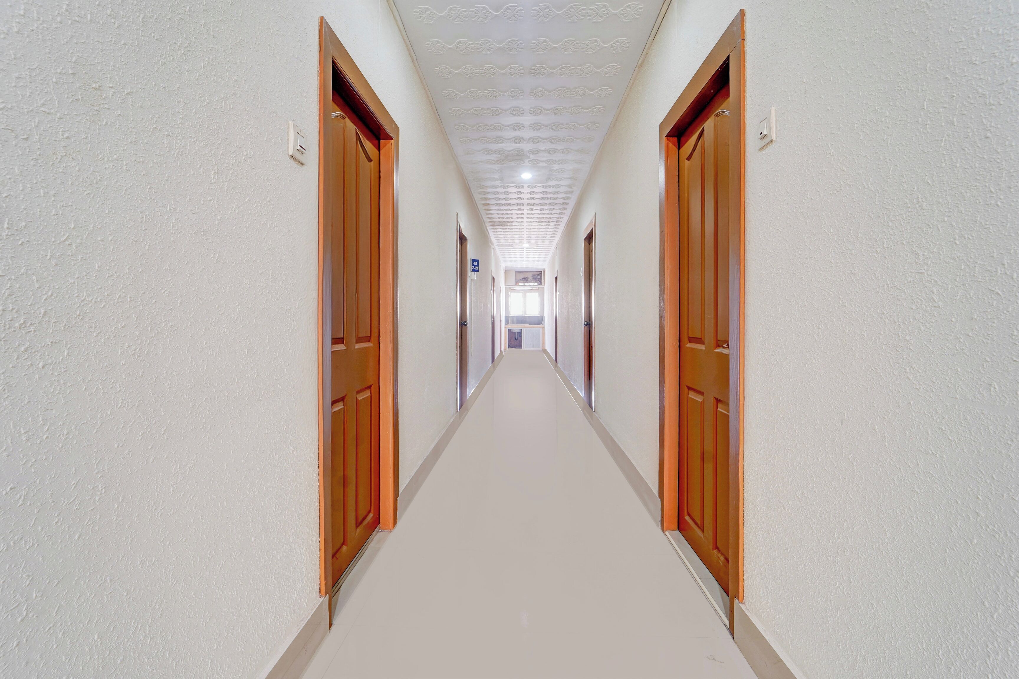 A long, narrow hallway with wooden doors on both sides, leading to a bright room at the end.