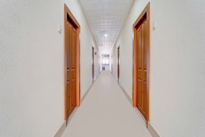 Un pasillo largo y estrecho con puertas de madera a ambos lados, que da a una habitación luminosa al final.
