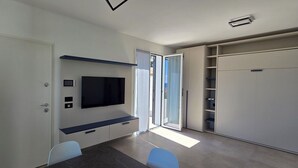 A modern room with a flat-screen TV mounted on the wall, a sliding door leading to a balcony, and built-in shelving units. - Nice apartment in villa with WIFI, A/C, TV, patio and panoramic view, close to Imperia (San Bartolomeo Al Mare)