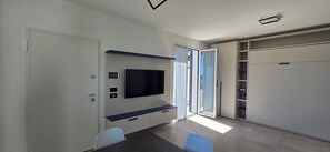 Ein modernes Zimmer mit flachbildfernseher an der Wand, einer Schiebetür, die auf einen Balkon führt, und eingebauten Regale.
