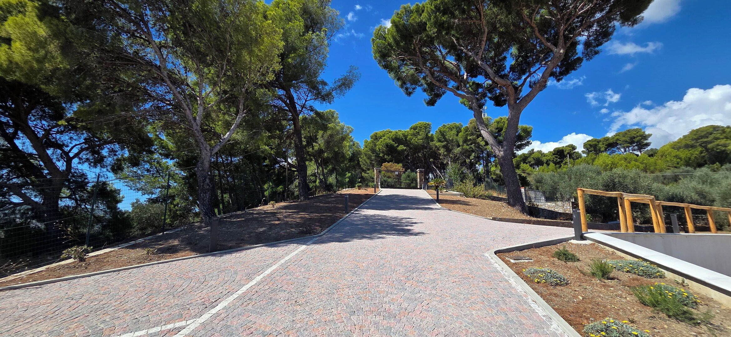 Un chemin pavé, bordé d’arbres, mène à un portail.