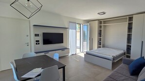 A modern living room with a flat-screen TV, a dining table, and a sofa. - Nice apartment in villa with WIFI, A/C, TV, patio and panoramic view, close to Imperia (San Bartolomeo Al Mare)