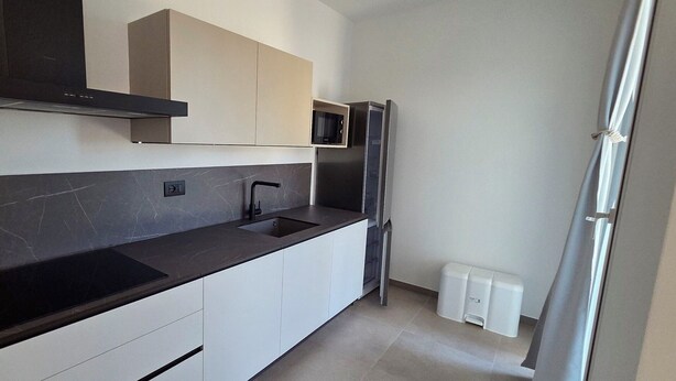 A modern kitchen with a black countertop, white cabinets, a stainless steel refrigerator, and a microwave. - Nice apartment in villa with WIFI, A/C, TV, patio and panoramic view, close to Imperia (San Bartolomeo Al Mare)