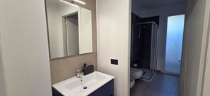 Un baño moderno con un lavamanos blanco, un espejo y una cabina de ducha.