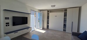 Ein modernes Wohnzimmer mit Flachbildfernseher, Einbauschränken und einer Schiebetür zum Kleiderschrank.