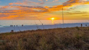 Una spiaggia al tramonto, con dune erbose e alcune persone che passeggiano.
