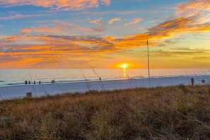 A beach with a sunset, grassy dunes, and a few people walking. - 19th Floor Gulf Views | 2 King Suites | Splash Resort East Tower (Panama City Beach)