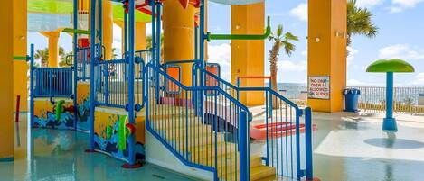 A water park with a colorful play structure, a no one over 14 allowed sign, and a view of palm trees and the sky.