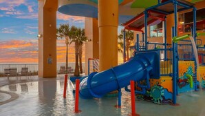 Un parco acquatico con uno scivolo blu, palme e vista sul tramonto.