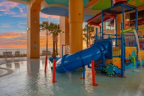A water park with a blue slide, palm trees, and a sunset view. - 19th Floor Gulf Views | 2 King Suites | Splash Resort East Tower (Panama City Beach)