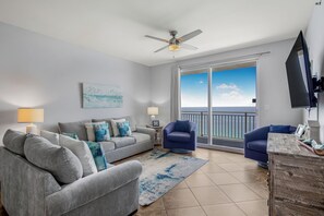 A living room with a grey sofa, blue armchairs, a ceiling fan, and a view of the ocean through large sliding doors. - 19th Floor Gulf Views | 2 King Suites | Splash Resort East Tower (Panama City Beach)