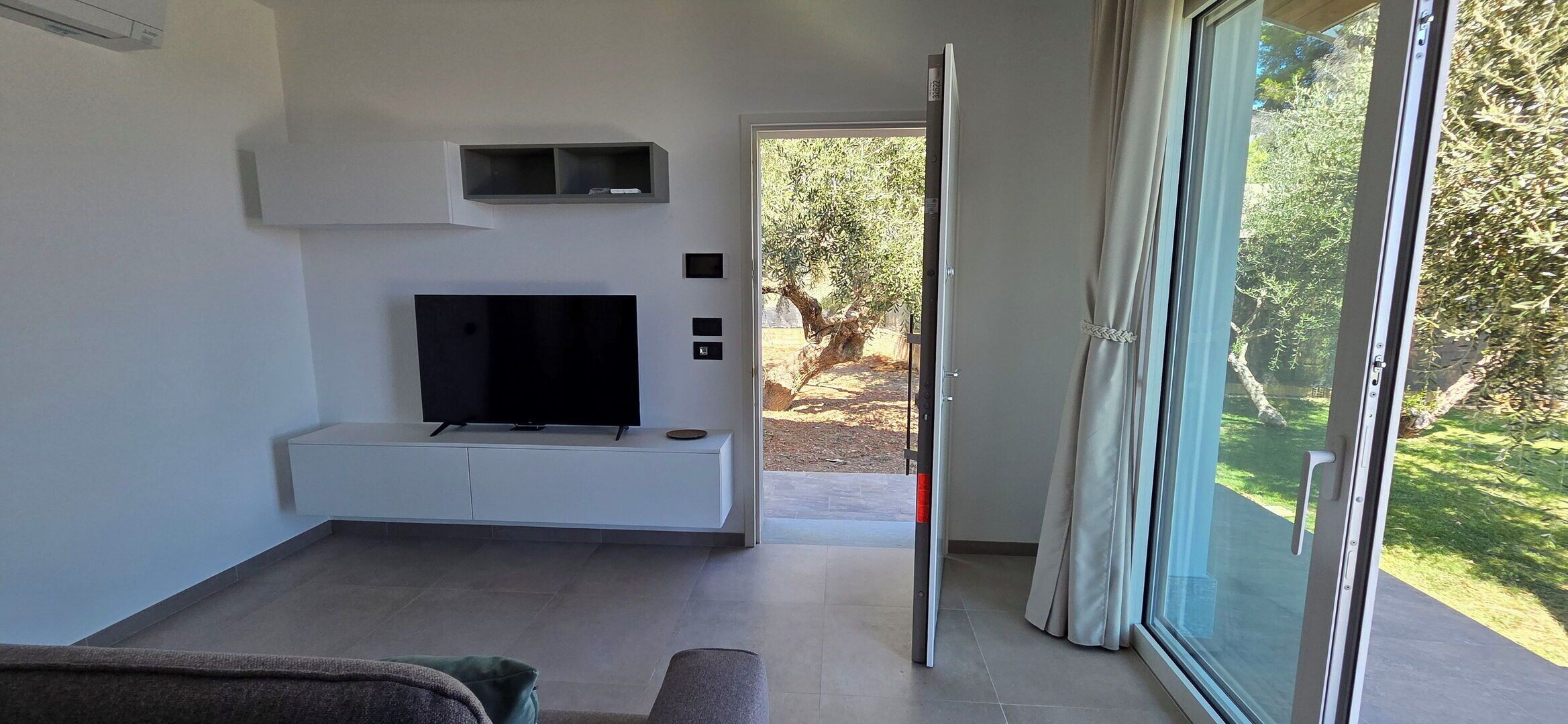 Een moderne woonkamer met een flatscreen televisie, inbouwplanken en een schuifdeur naar een buitenruimte.
