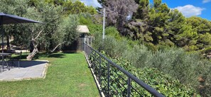Eine Terrasse mit Tisch und Stühlen, ein überdachter Sitzbereich und Blick auf einen Garten mit Metallzaun.