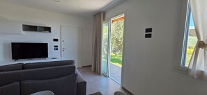 Ein modernes Wohnzimmer mit Flachbildfernseher, grauem Sofa und einer Schiebetür zu einem Garten.