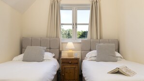 Ein Doppelzimmer mit zwei Betten, einem Nachttisch, einer Lampe und einem Fenster mit Vorhängen.