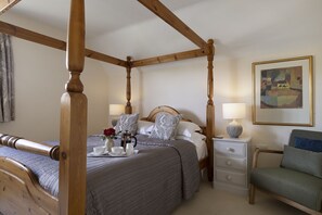 A four-poster bed with a bedside table, a chair, a painting on the wall, and a bedside lamp. - Birch House -  a cottage that sleeps 8 guests  in 4 bedrooms (Stow-on-the-Wold)