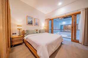 Een slaapkamer met een bed, nachtlampjes, een raam en uitzicht op een balkon.