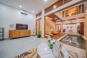 A spacious living area with a flat-screen TV, a wooden entertainment unit, a guitar, and a pool. - 3BR Umalas Villa • Pool & Rooftop Terrace • Scooter & Restaurant discounts (Kuta Utara)