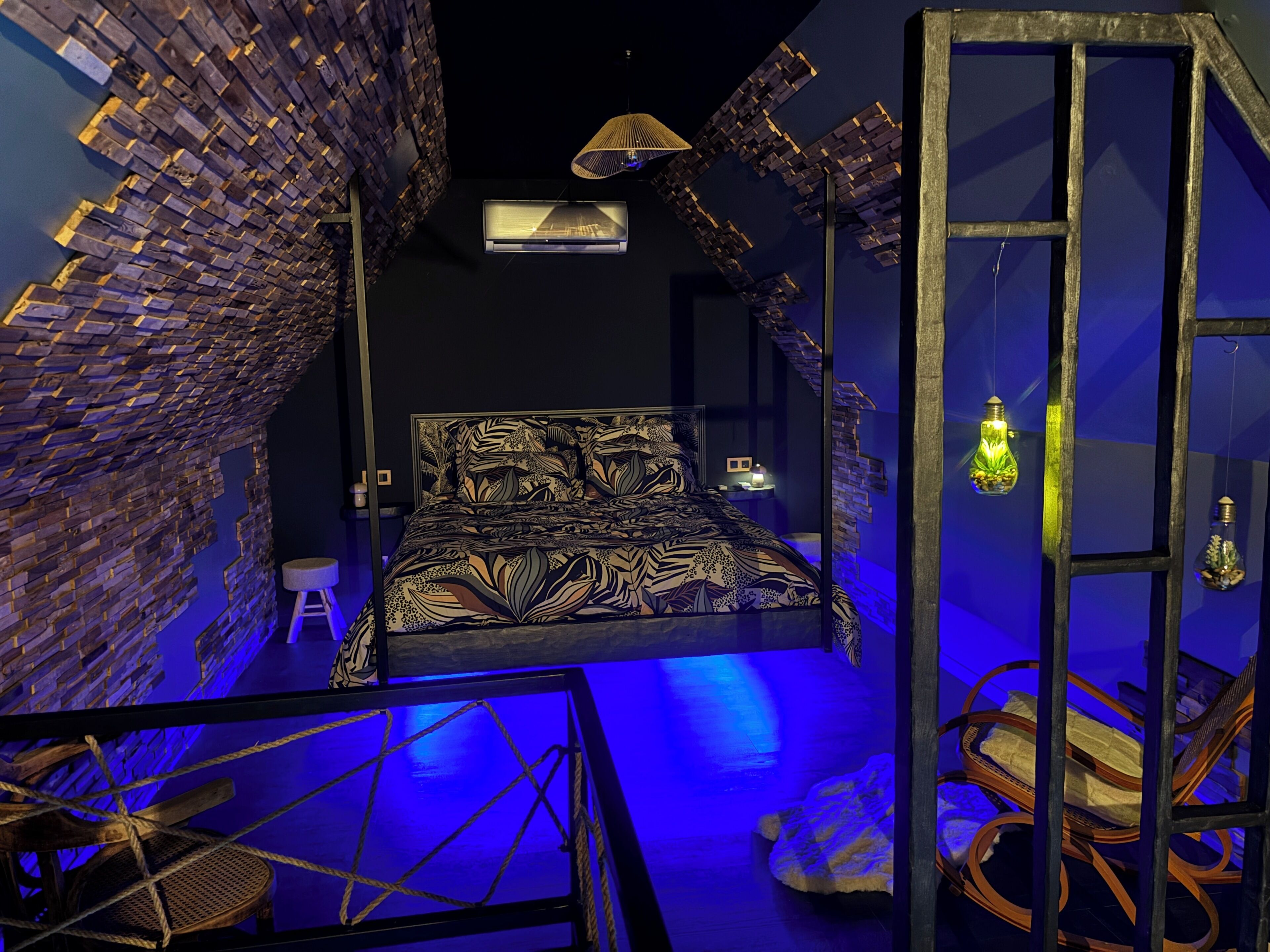 A room with a bed, a chair, a hanging light fixture, and a wall with a brick pattern.