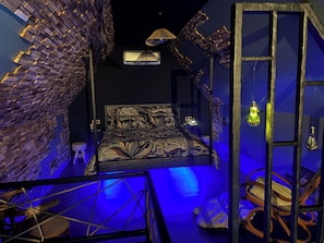 Quarto com uma cama, uma cadeira, luminária pendente e parede com padrão de tijolos.